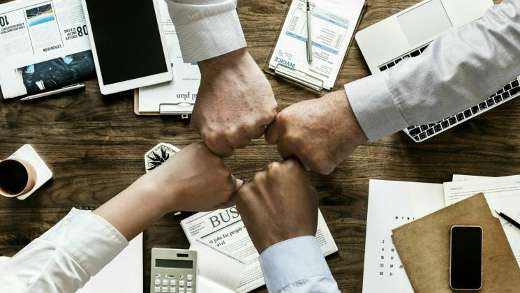 Four fists fistbumping above documents, office supplies, etc