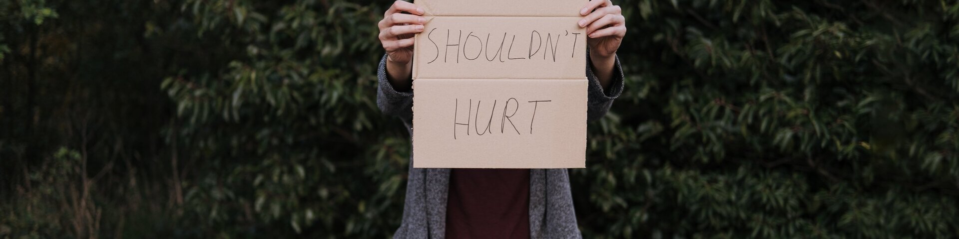 A person holding out a cardboard sign that says "Love shouldn't hurt"